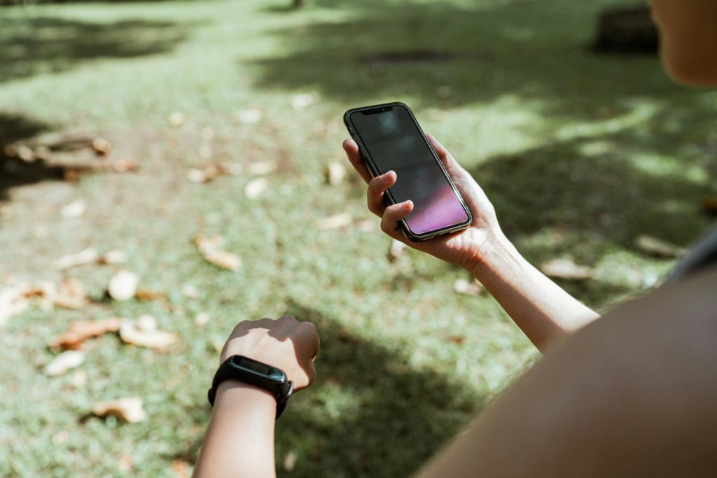From above crop unrecognizable female wearing fitness tracker browsing modern mobile phone with blank screen while resting in green park